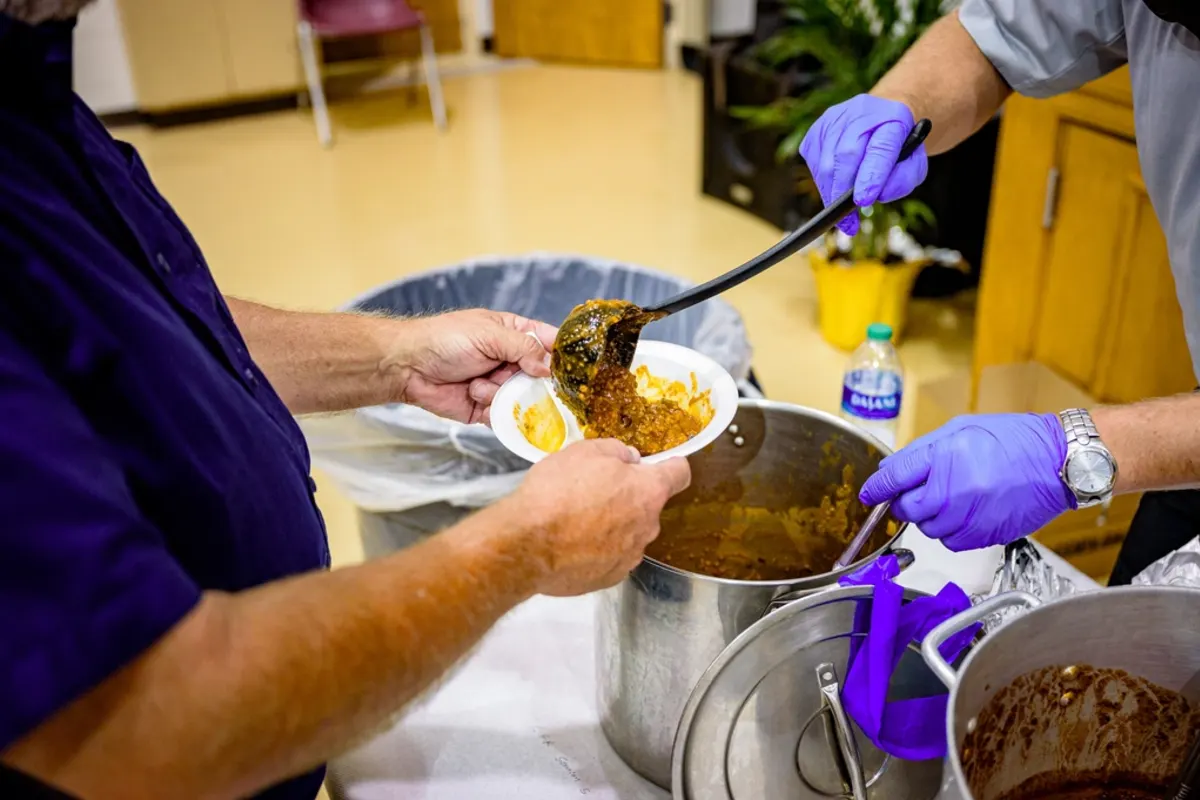 A volunteer in gloves ladling a hot meal into a bowl